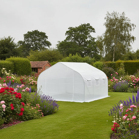 White walk-in polytunnel in a traditional English cottage garden surrounded by roses, lavender and colourful flower borders with a brick outbuilding in the background